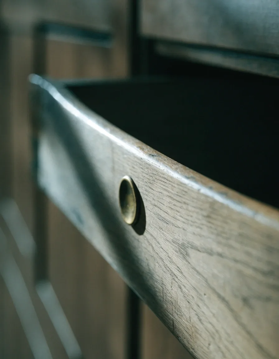 Close view of a worn oak card drawer edge with a brass pull under low raking light